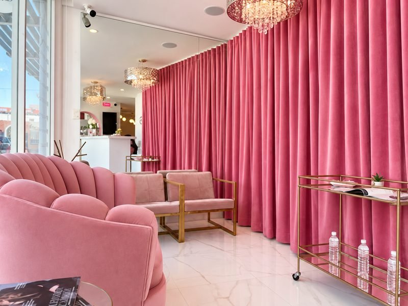 Sala de espera de Twin Brows con sillones de terciopelo rosa, cortinas y candelabros